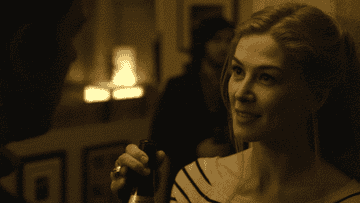 Rosamund Pike in Gone Girl, holding a bottle and chuckling.