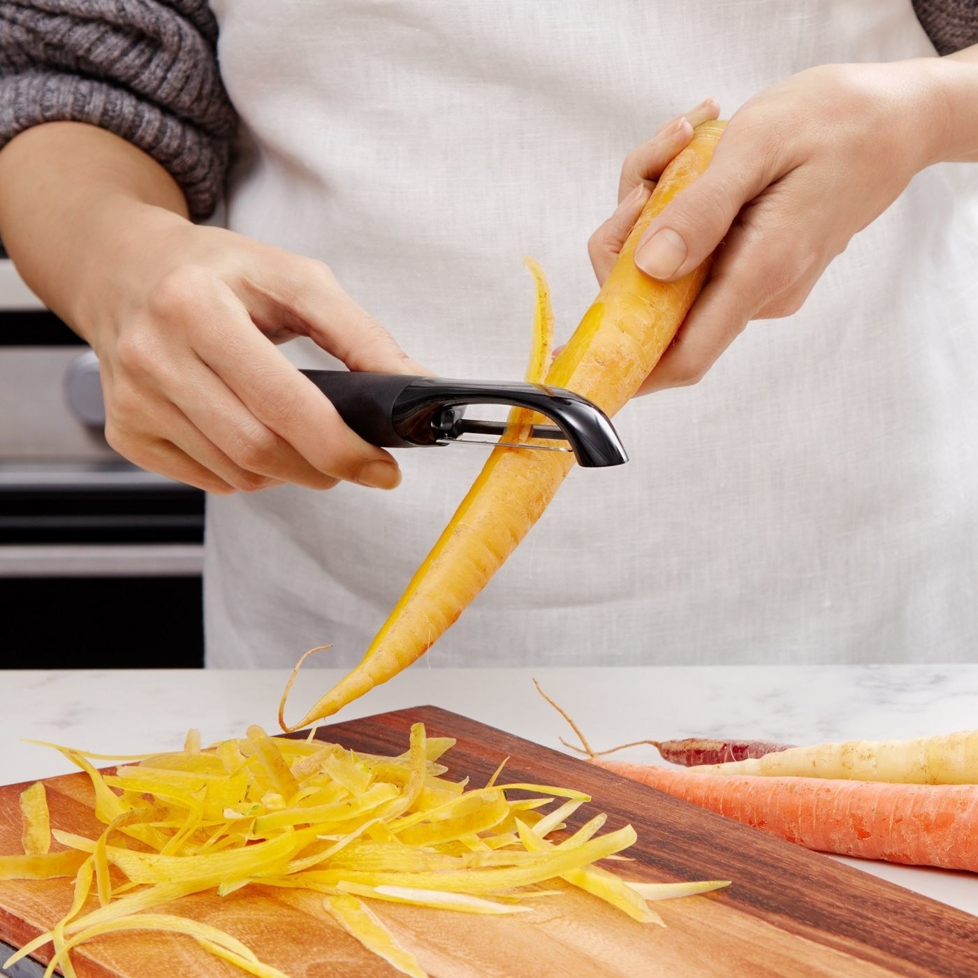model holding a black peeler peeling carrots over a cutting board