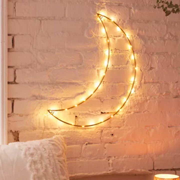 A crescent moon-shaped light sculpture on a rustic brick wall