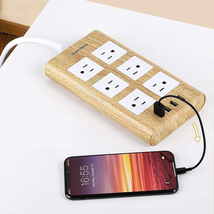 A phone plugged into the power bar; it looks like its made of wood
