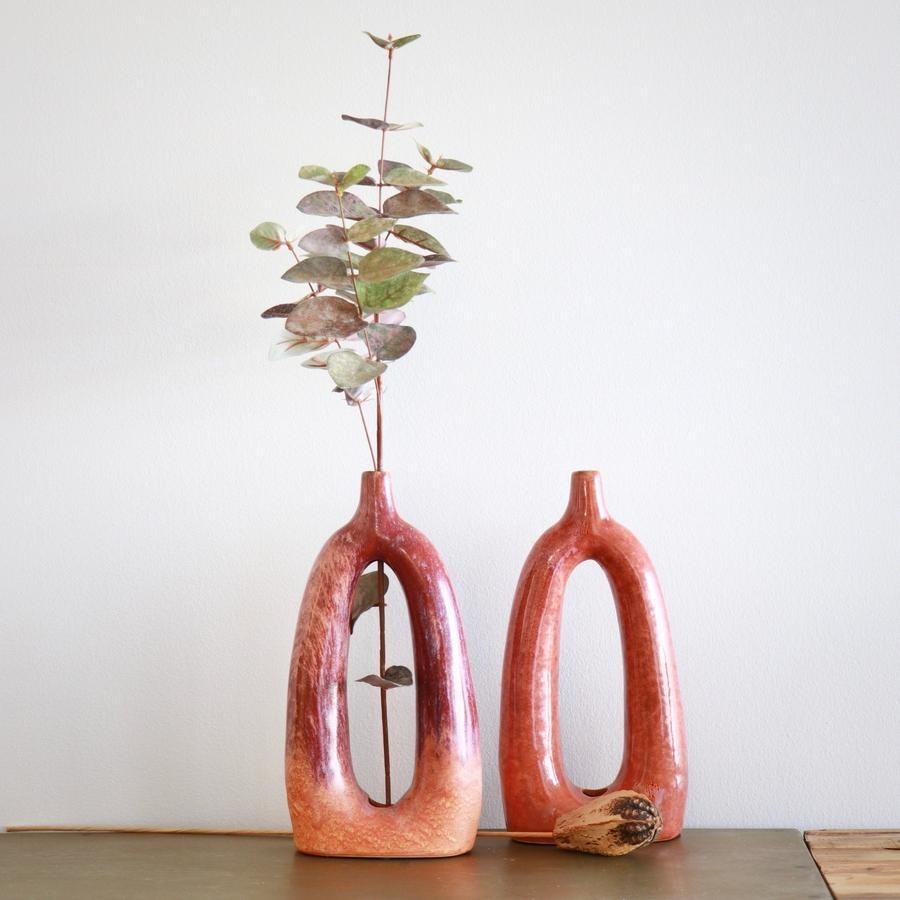 two persimmon colored vases, one with a long stem in it