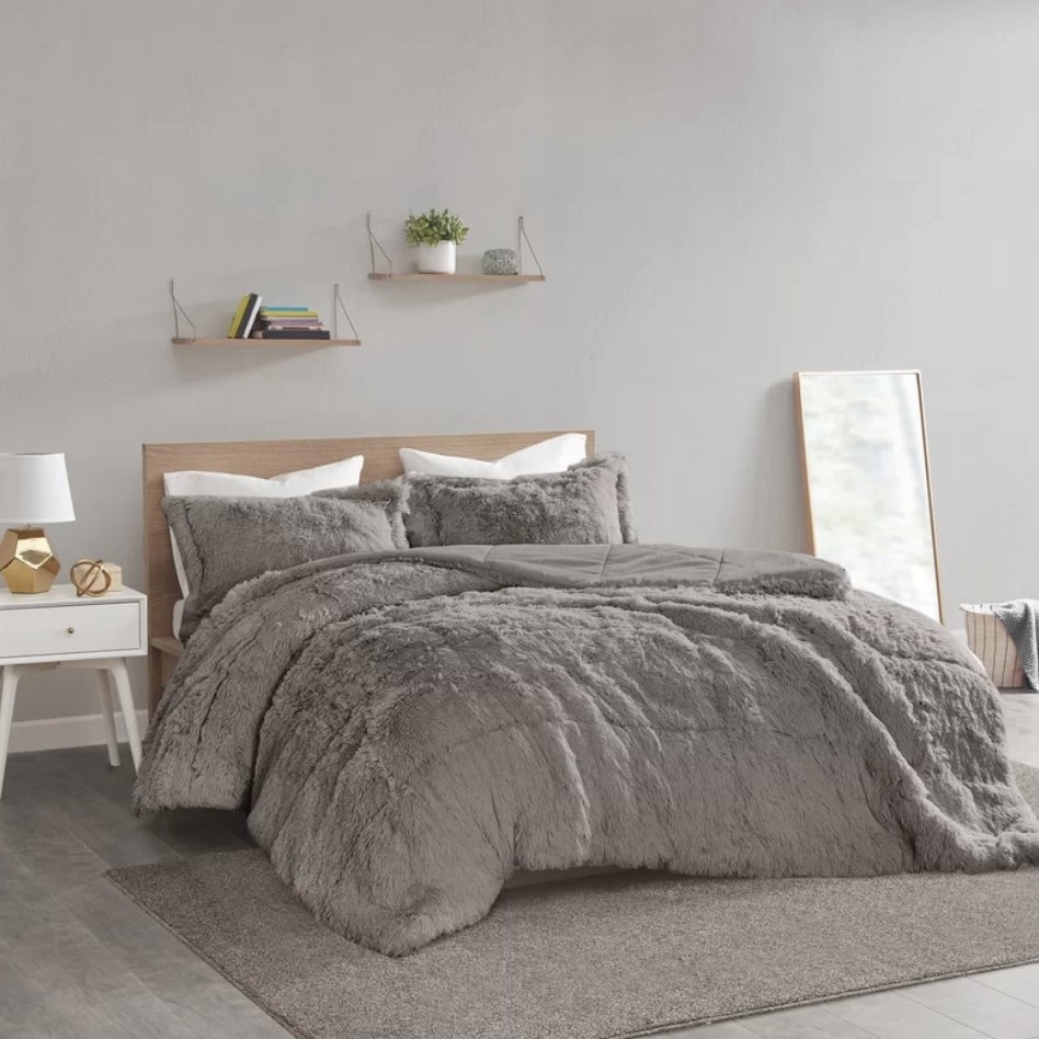 A gray, faux mink comforter with two matching pillows on a bed