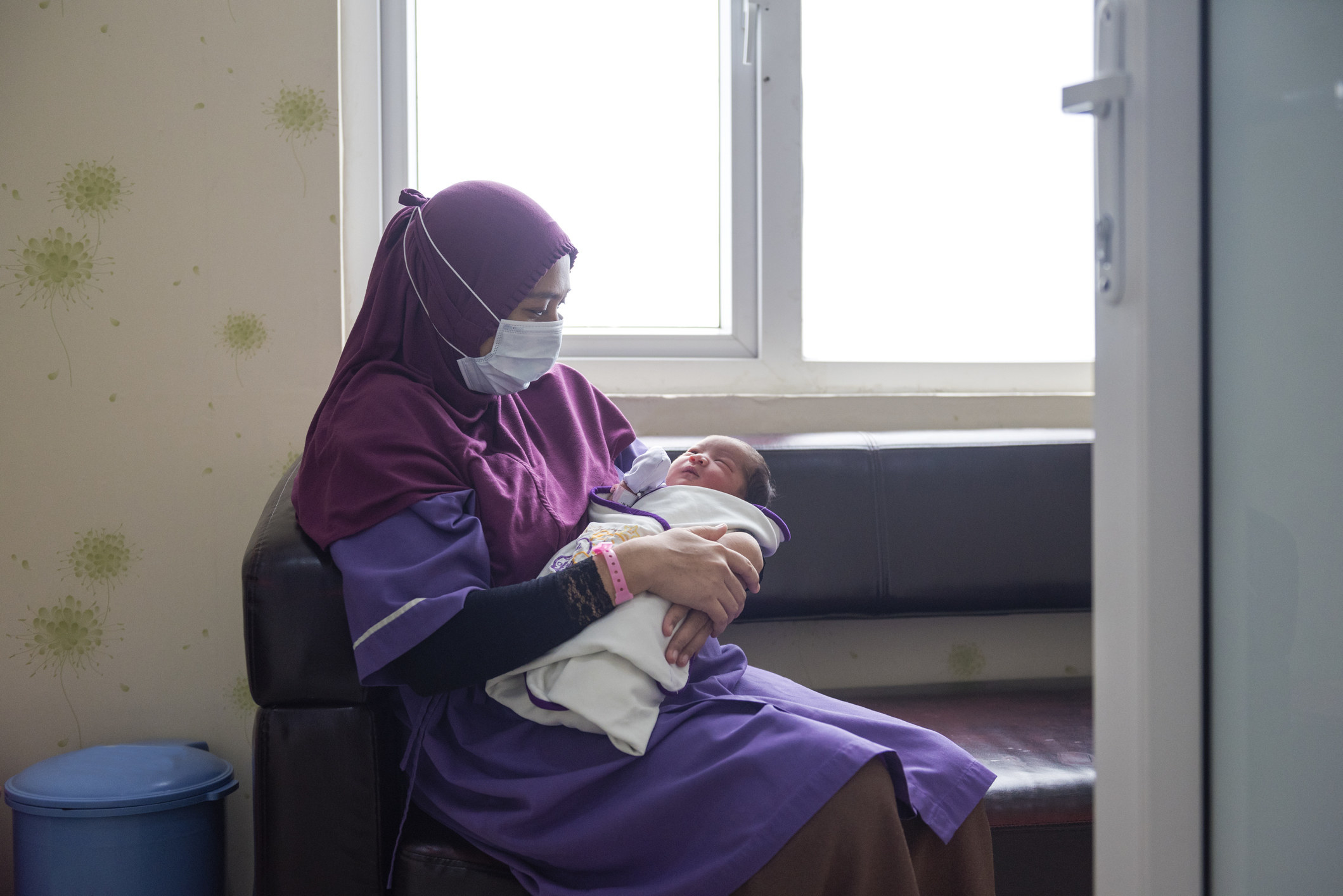 masked woman holding a newborn baby