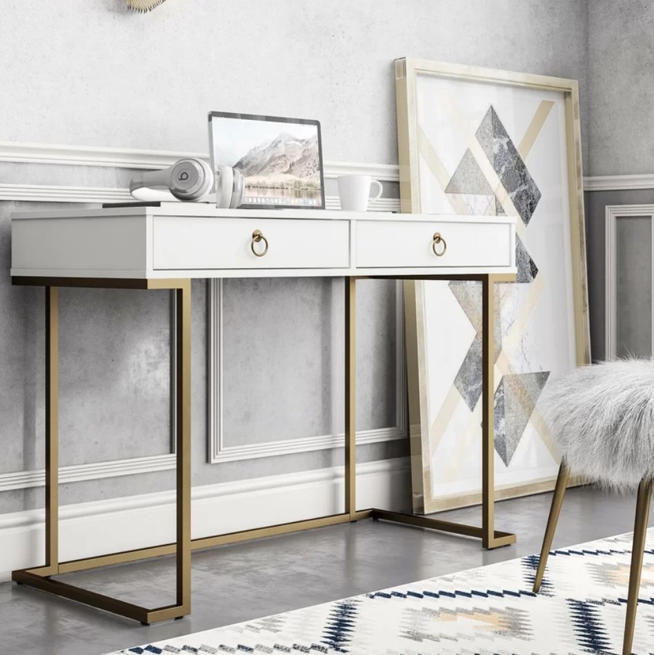 A white desk with a gold metal base and two drawers placed in a home office