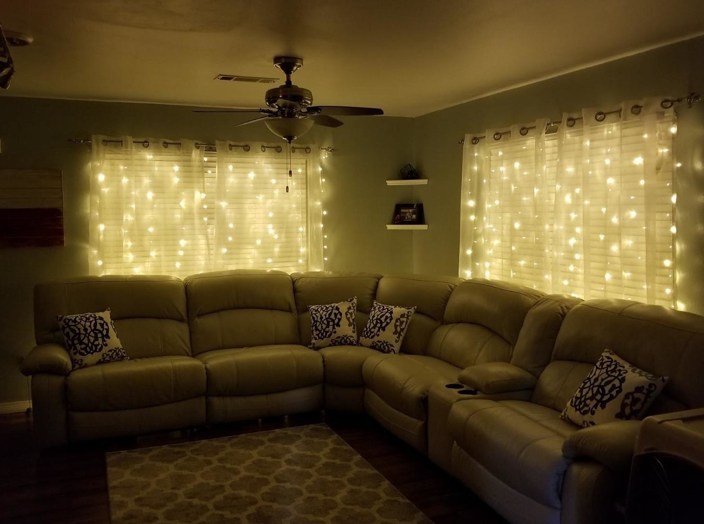 a reviewer photo of the string lights hanging behind sheer curtains in a darkened living room 
