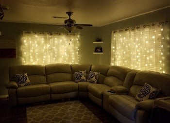 a reviewer photo of the string lights hanging behind sheer curtains in a darkened living room 