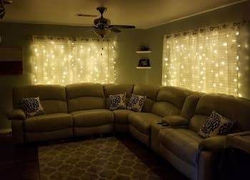 a reviewer photo of the string lights hanging behind sheer curtains in a darkened living room 