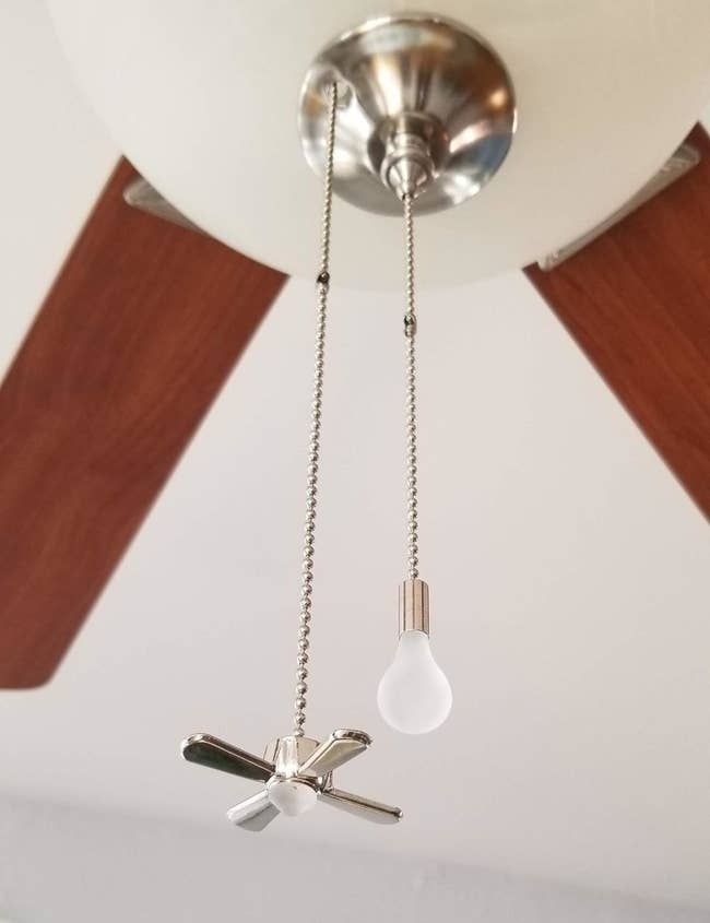 a reviewer photo of a fan with two fan chains attached with a small fan on one end and a small lightbulb on the other end