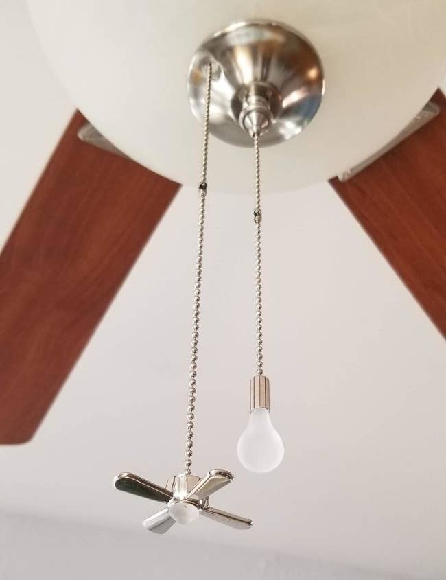 a reviewer photo of a fan with two fan chains attached with a small fan on one end and a small lightbulb on the other end