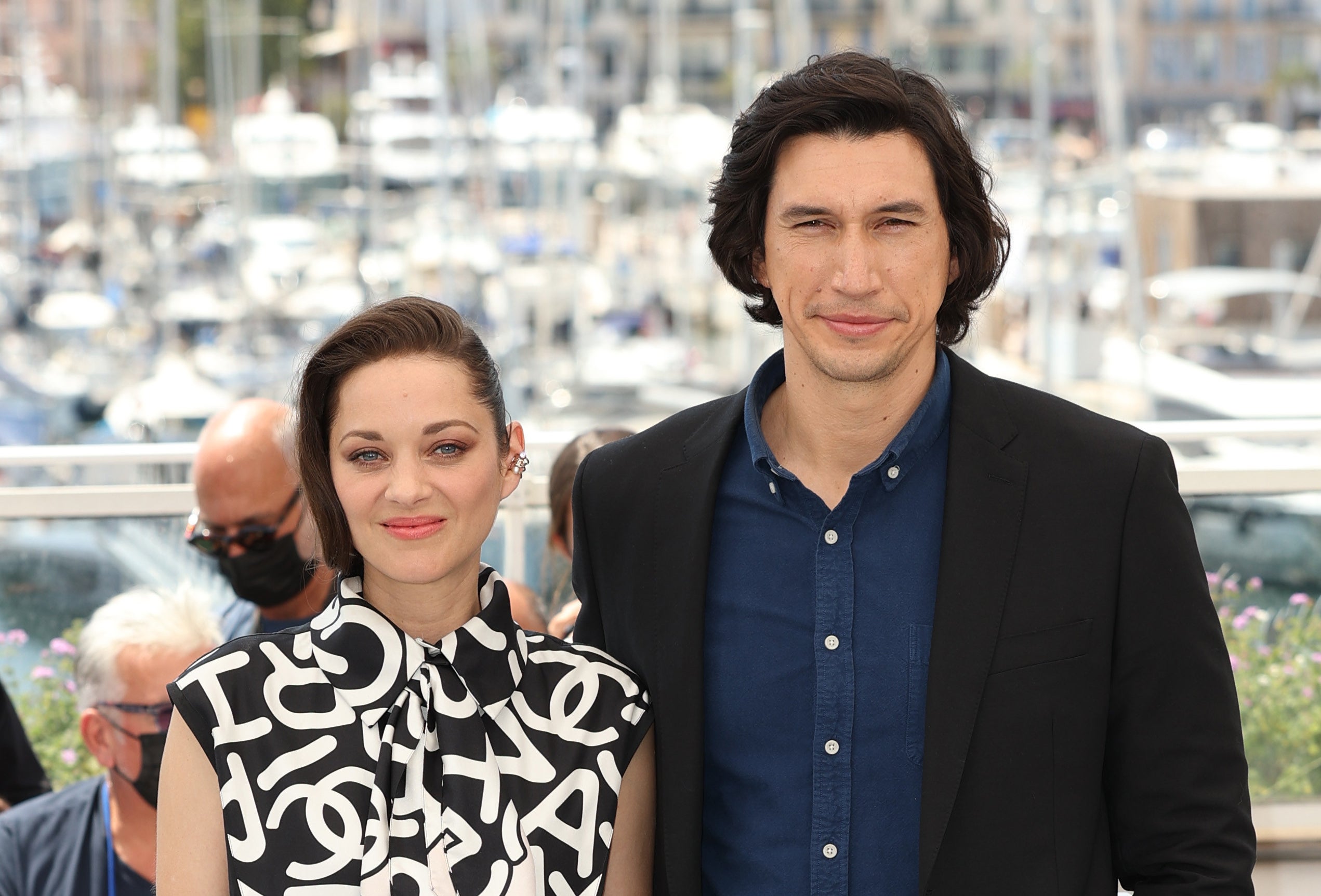 Photo of Marion Cotillard and Adam Driver from the waist up. They&#x27;re both smiling at the camera. She&#x27;s wearing a black and white sleeveless collared shirt and he&#x27;s wearing a dark blue button-up shirt and black suit jacket.