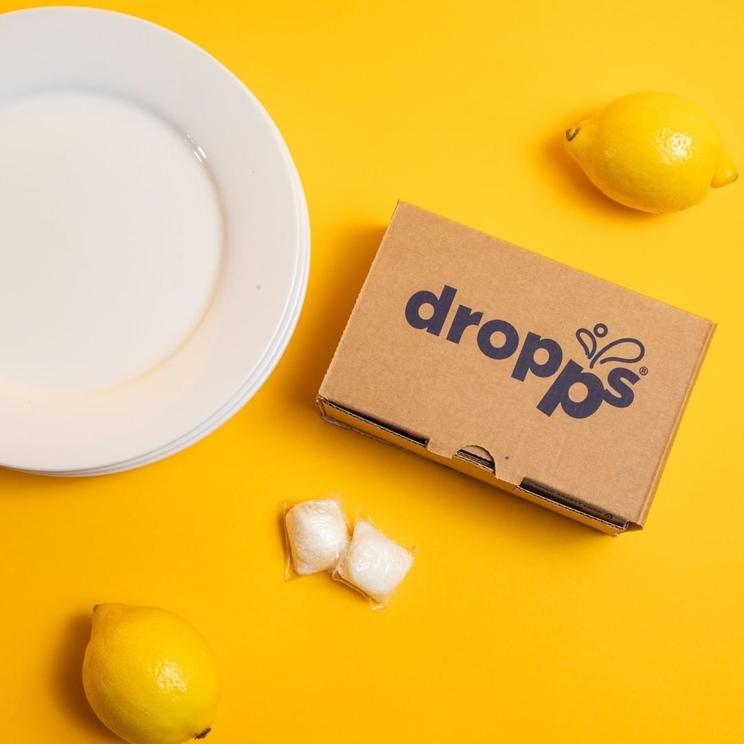 the dropps box, two pods, two lemons, and two plates against a bright yellow background