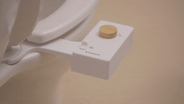 A person turning a knob and water spraying out of the bidet attachment on a toilet