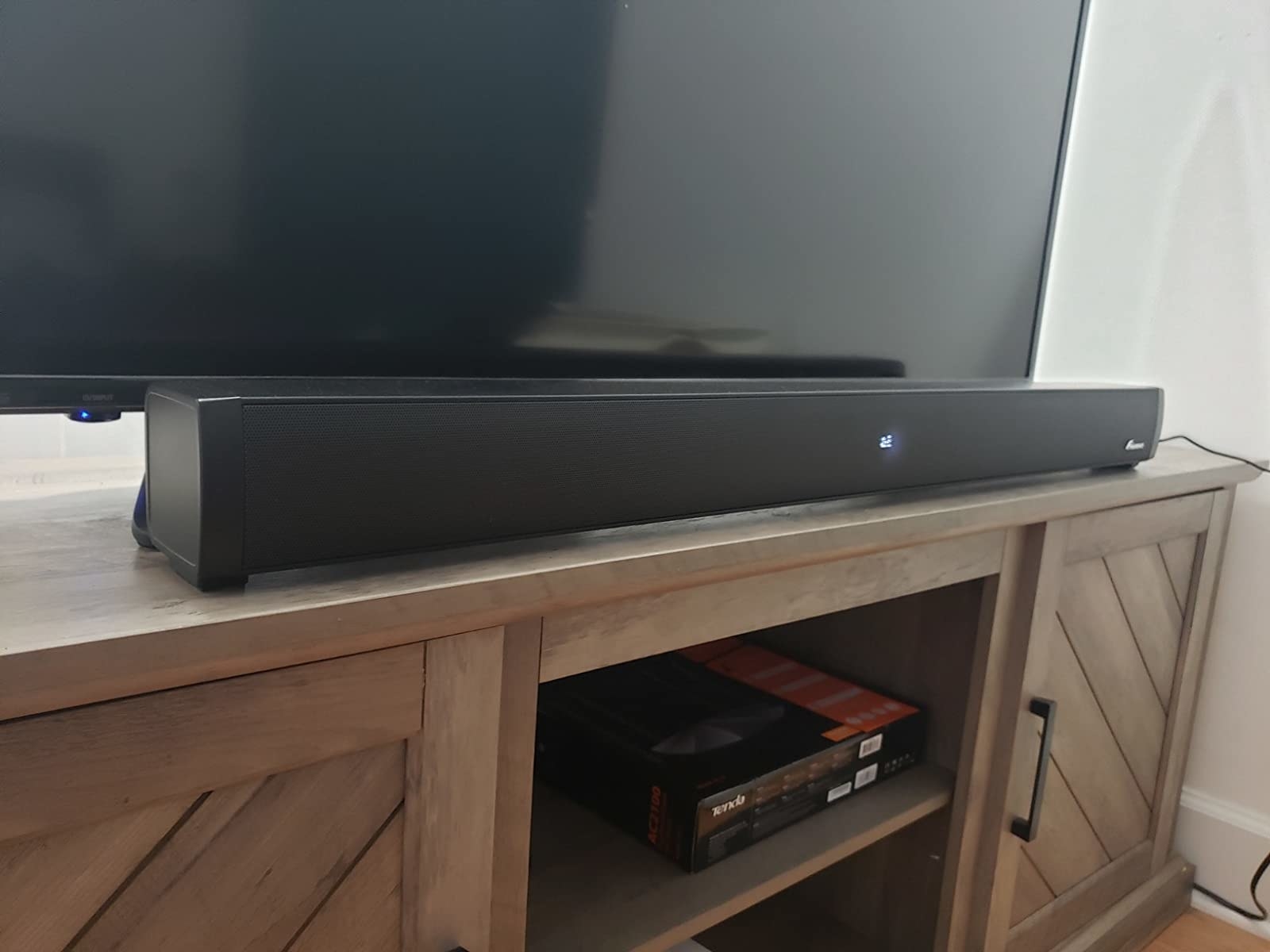 reviewer image of the foxnovo sound bar next to a TV on a TV stand