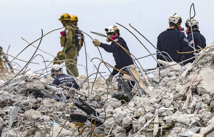 Rescuers wearing masks and helmets stand in the twisted rubble