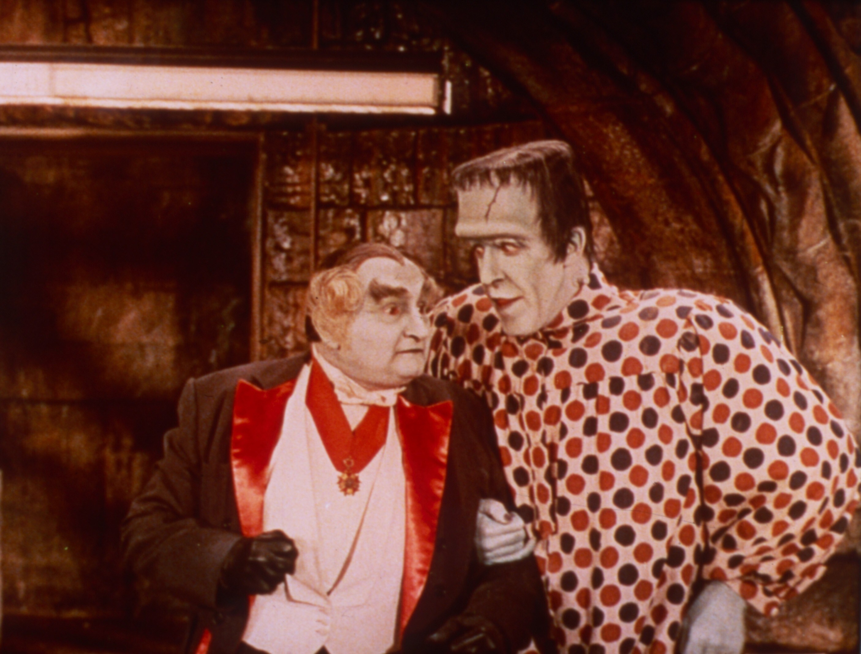 Al Lewis and Fred Gwynne stand next to each other dressed up as a vampire and Frankenstein