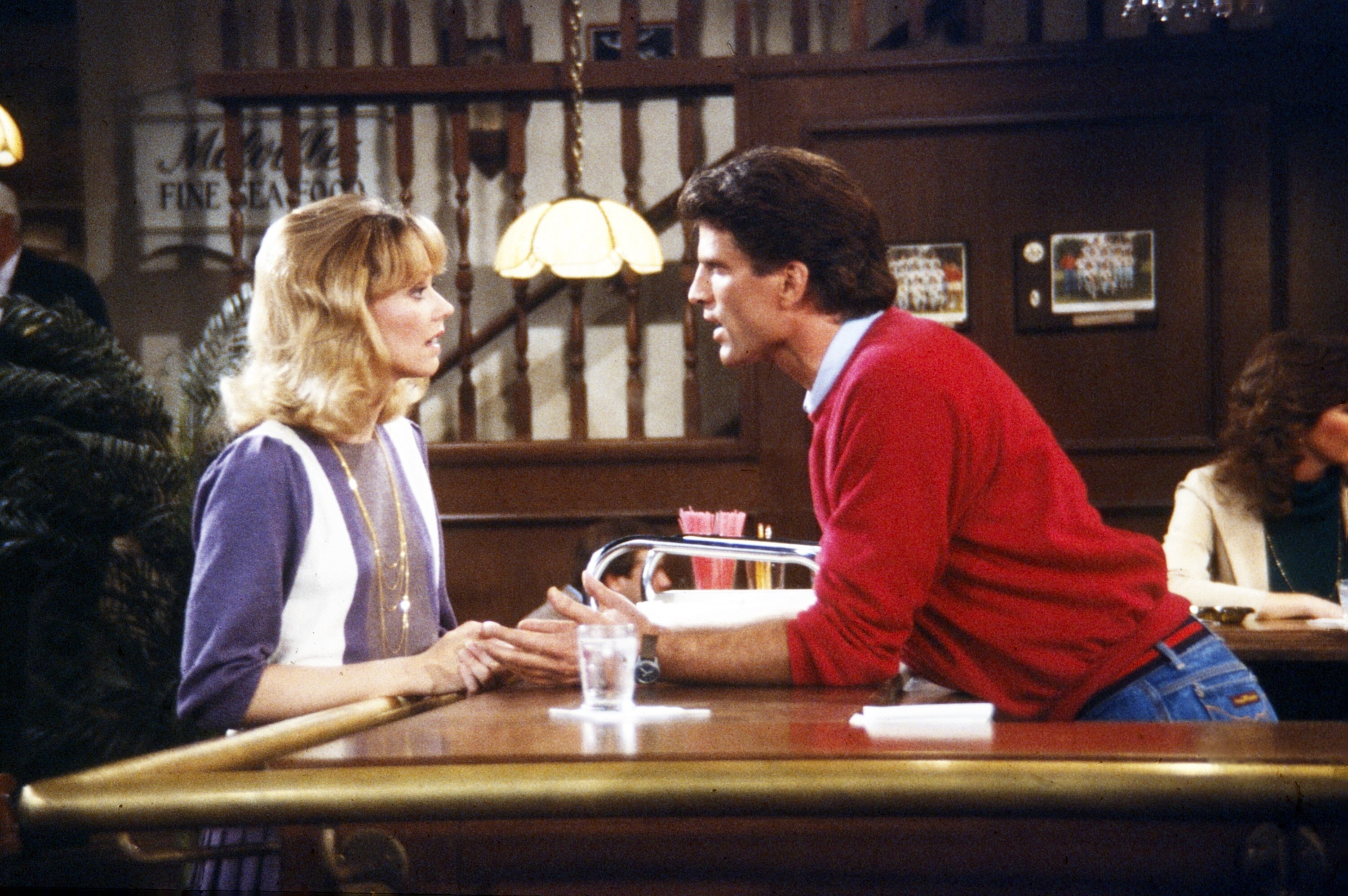 Shelley Long and Ted Danson lean on a bar looking at each other