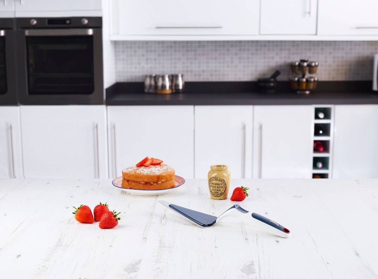 a cake slice server next to a cake and strawberries on a kitchen island