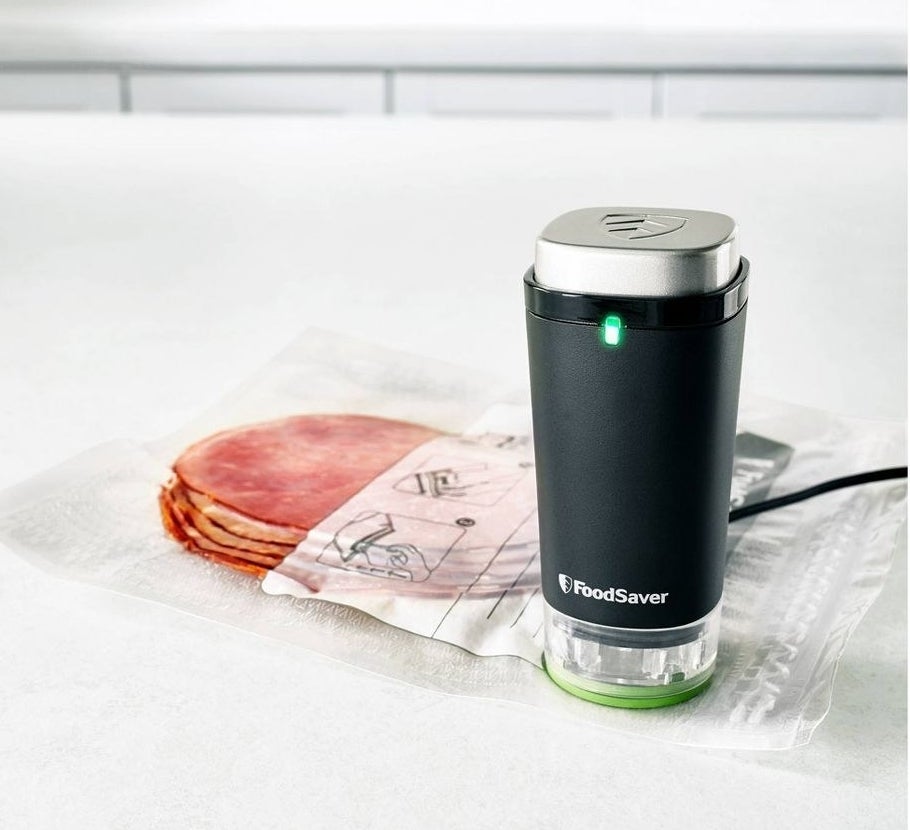 a small, handheld vacuum sealer vacuuming a plastic bag with cold cuts