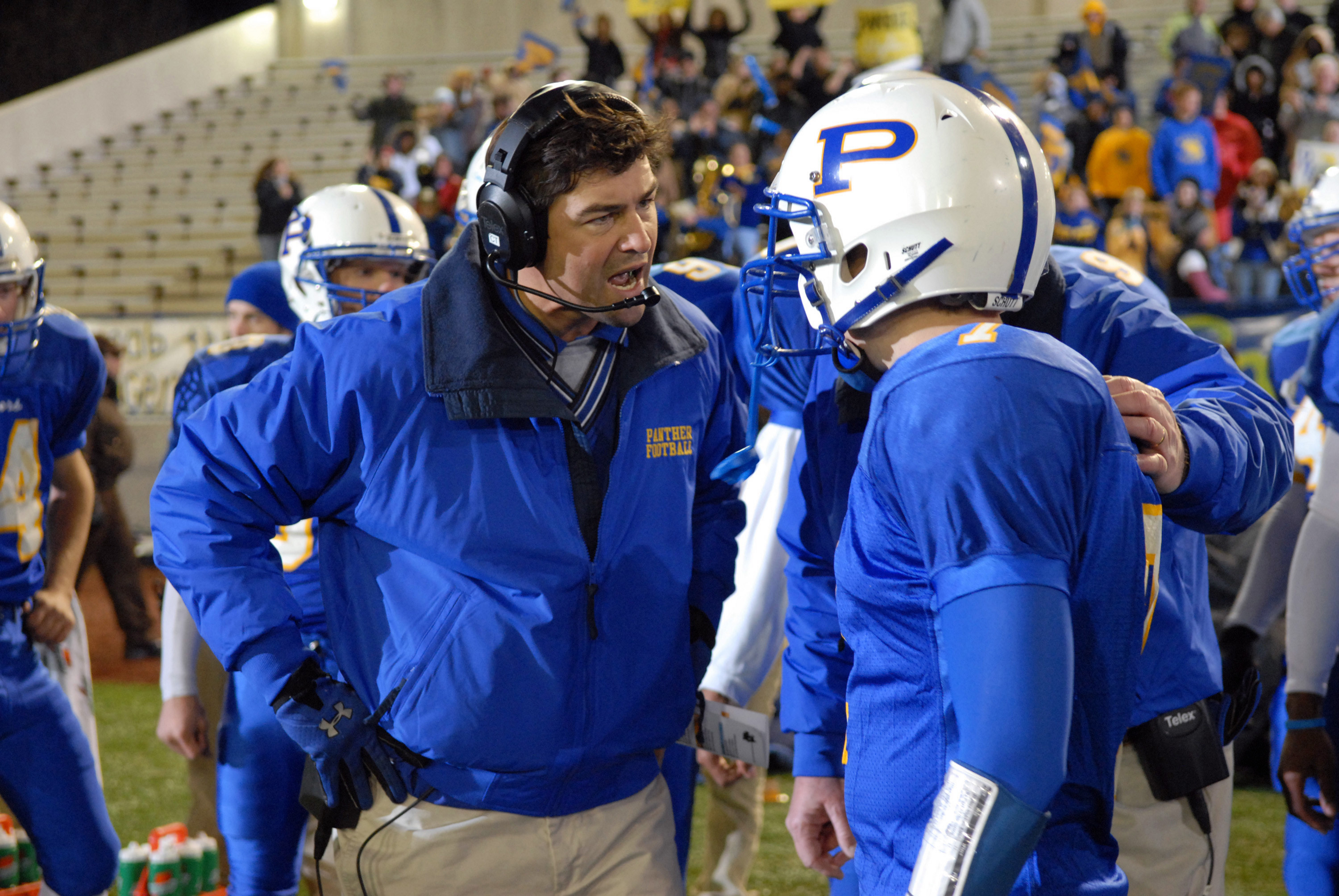 Kyle Chandler yells at Zach Gilford on the sidelines of a football field