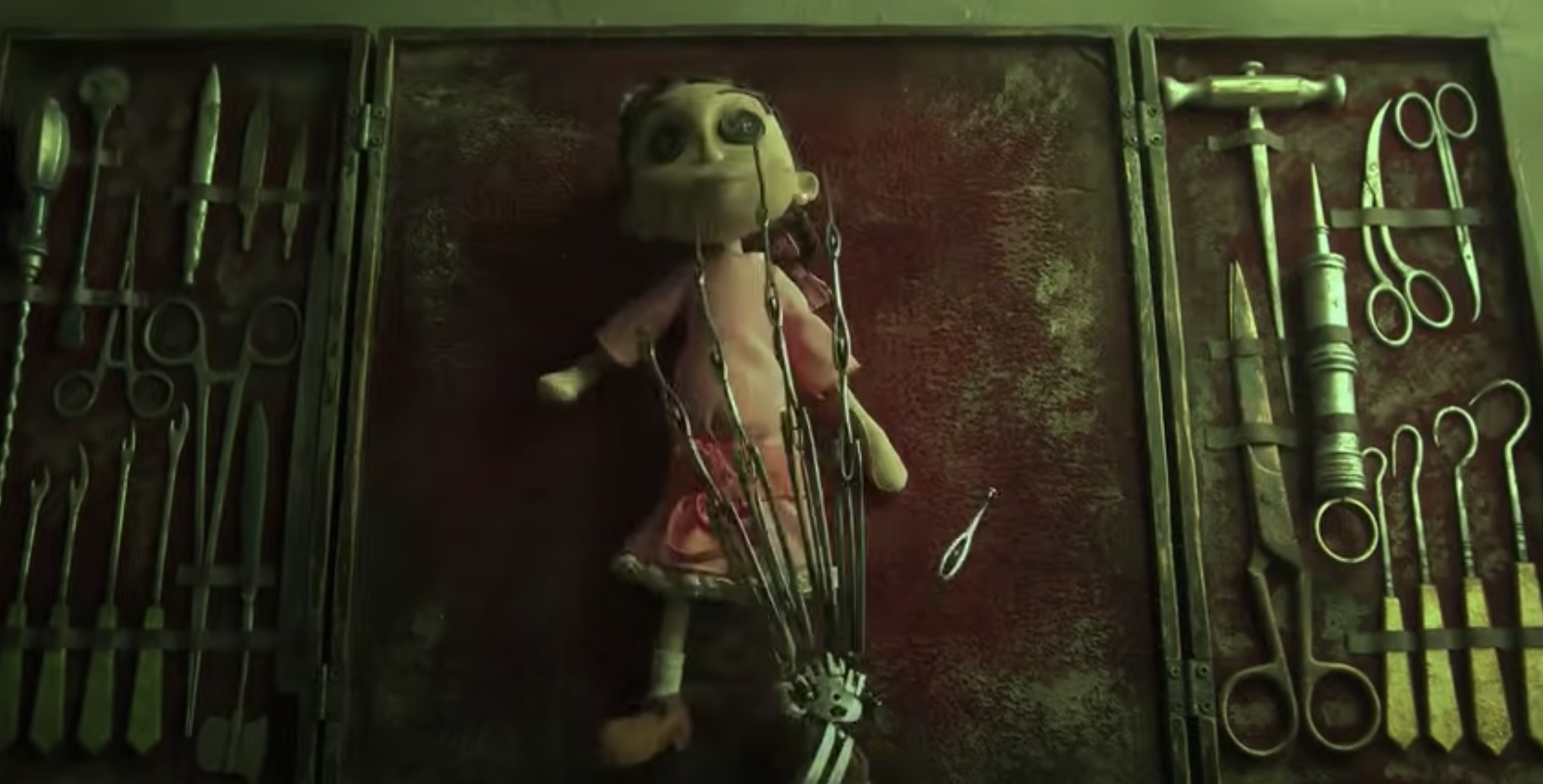 A metal hand hovers over a doll with button eyes