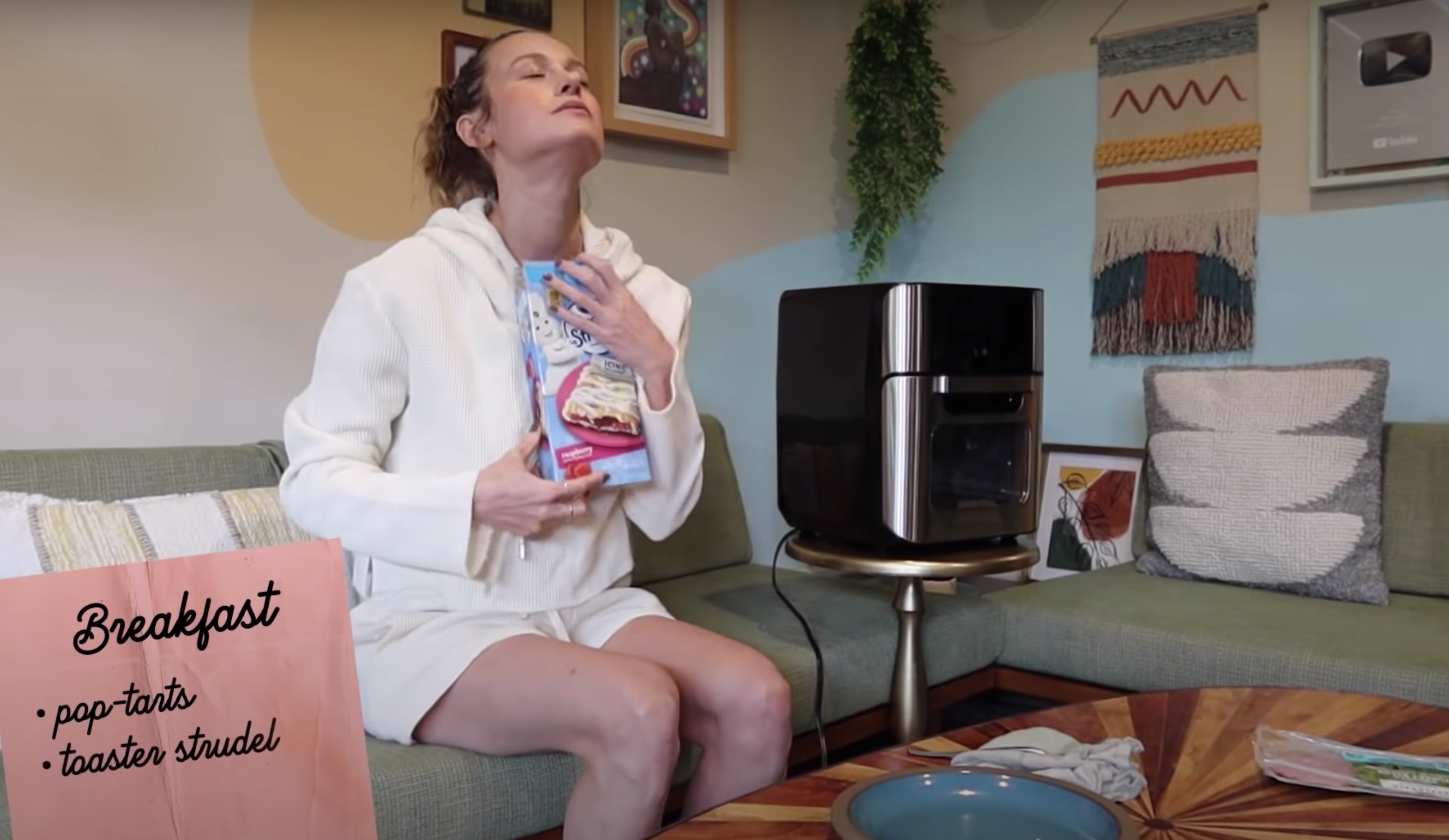 Brie holds a package of toaster strudels close to her while sitting next to her air fryer