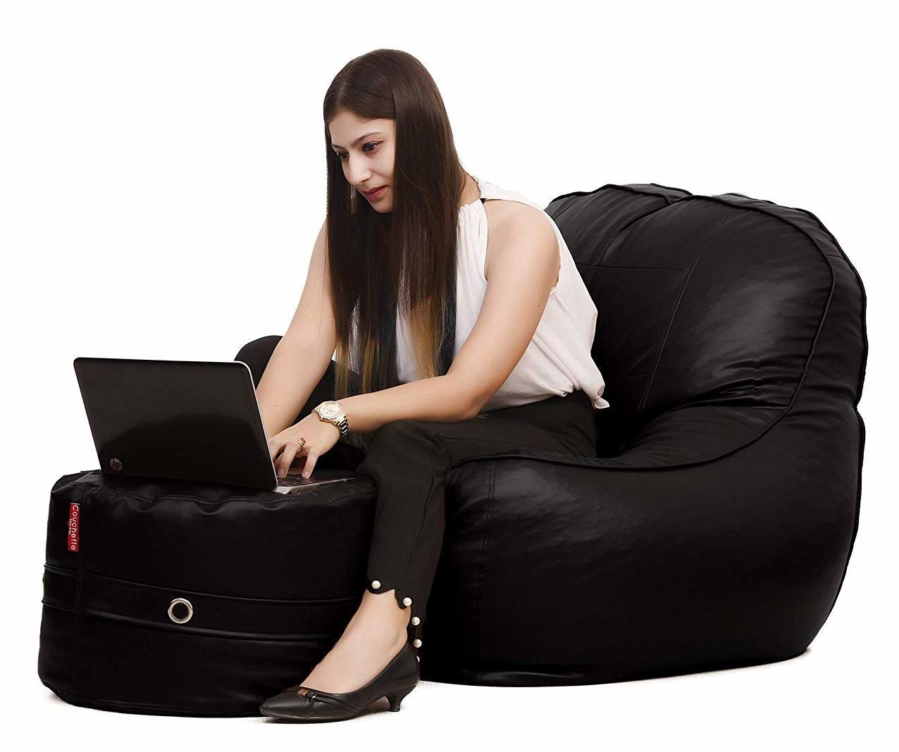 A woman sitting on a bean bag, working on a laptop that&#x27;s placed on the footrest