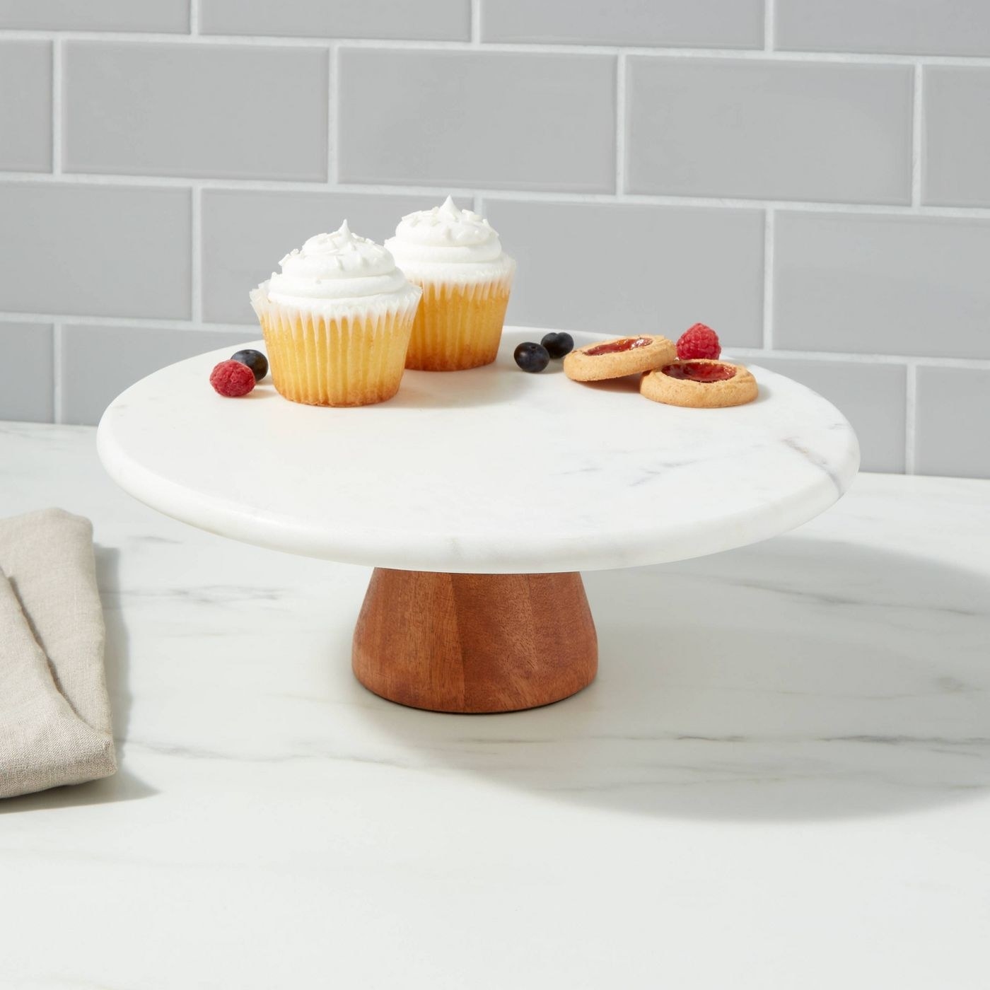 cupcakes and fruit on a marble cake stand with a wooden base