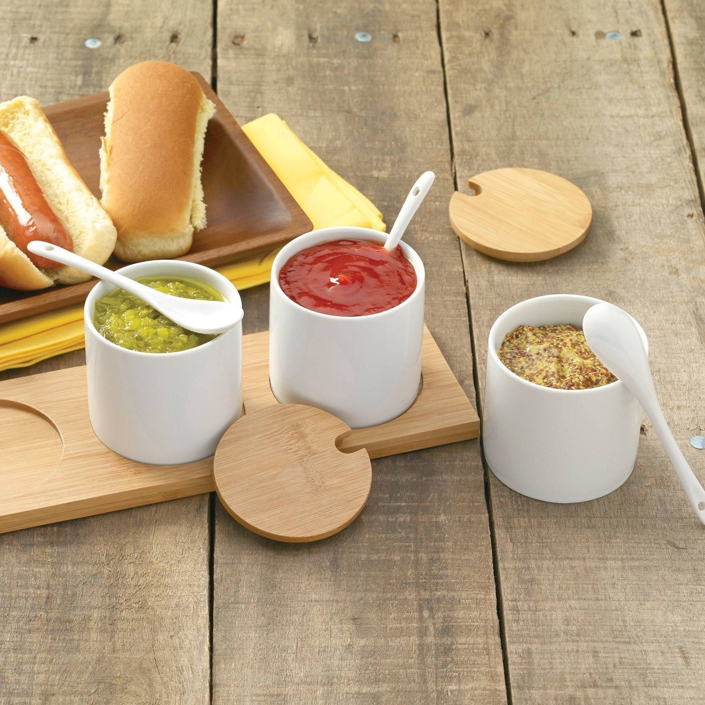 three white ceramic condiment jars with matching spoons, wooden lids and a wooden tray