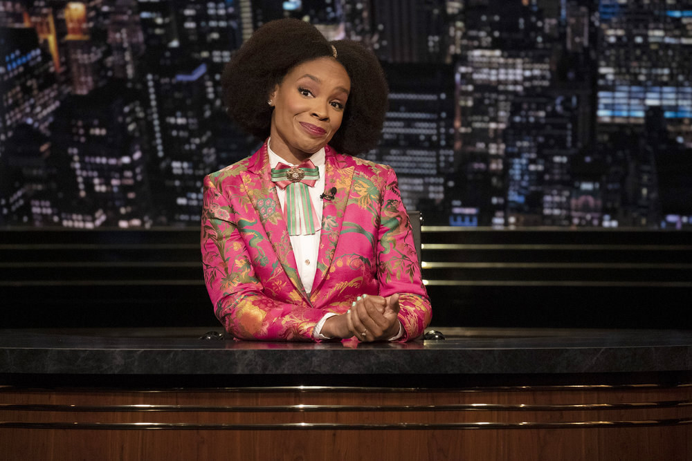 Amber Ruffin sits behind her late-night desk