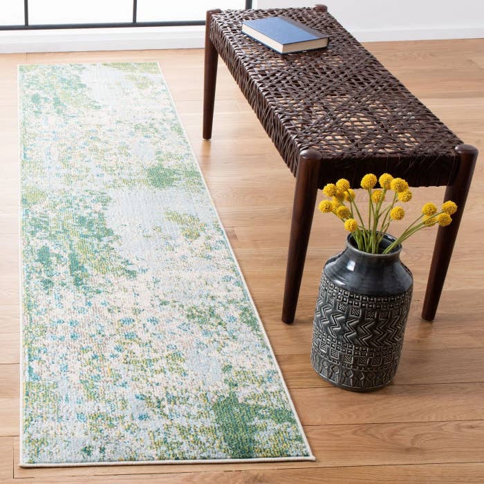 a green and blue runner rug next to a woven bench