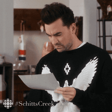 David from Schitt&#x27;s Creek looks down at a paper he&#x27;s holding, then back up in concern