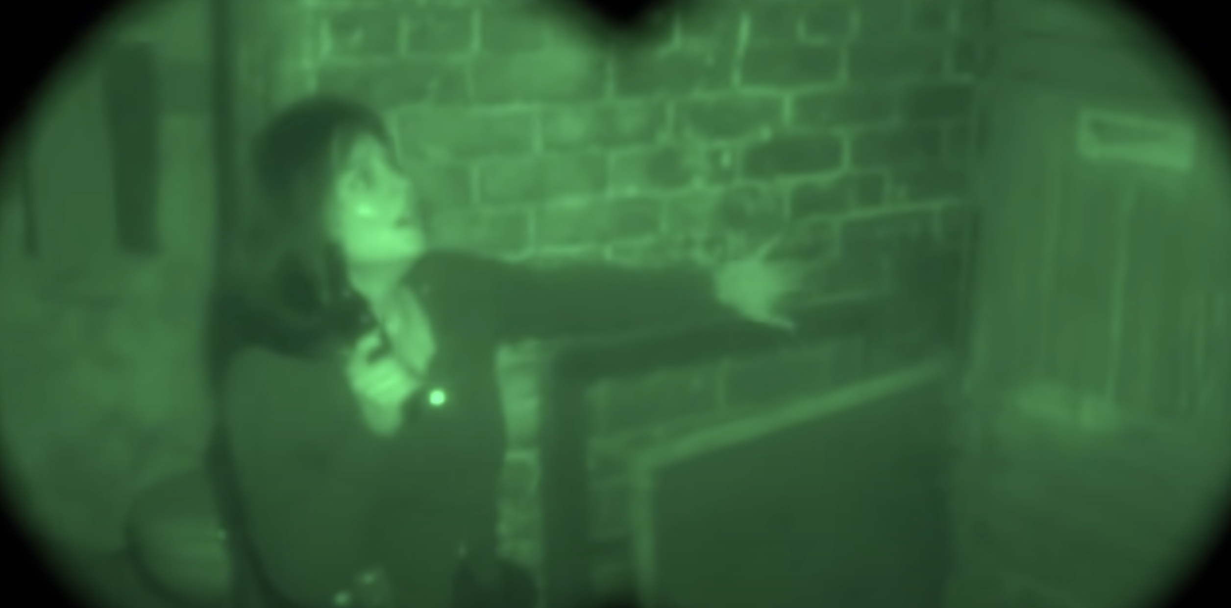A scared woman seen through night vision goggles grabs hold of the wall