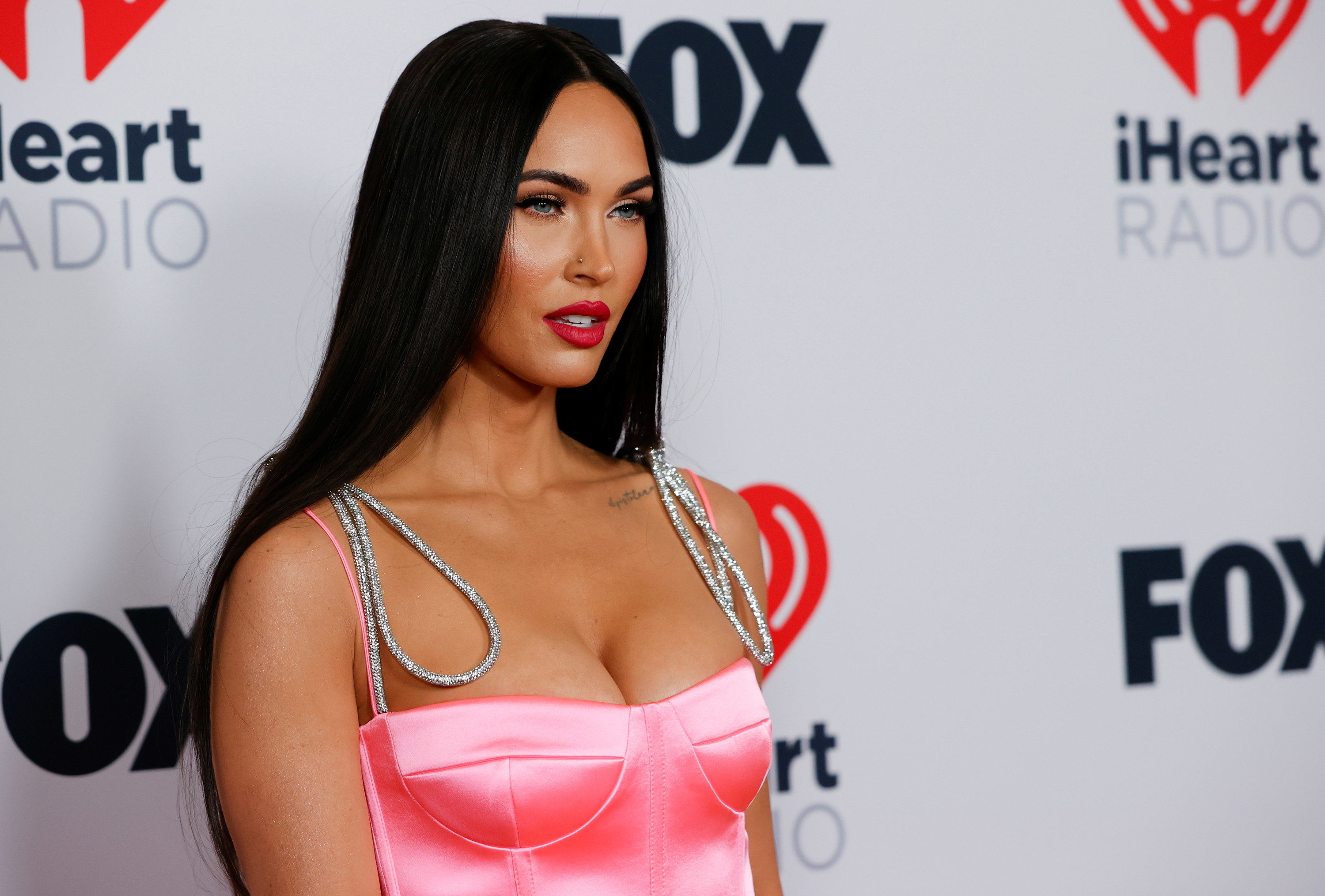 Photo of Megan Fox from the waist up in a satin pink dress with silver straps looking off-camera