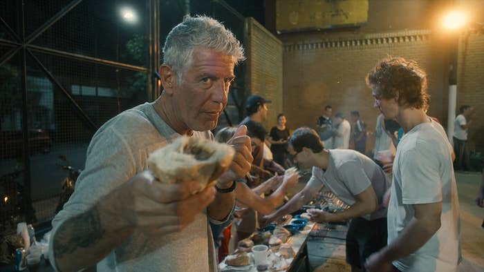 Bourdain holding a cheesesteak sandwich close to the camera