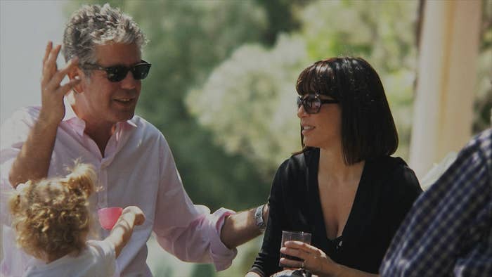 Bourdain and Ottavia Busia sitting outdoors in the sun with family