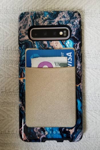 a reviewer photo of the adhesive pocket applied to the back of a phone and filled with a card and cash 