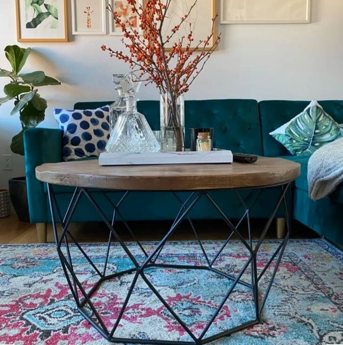 A reviewer&#x27;s round, wooden coffee table with a geometric metal base with decor items atop