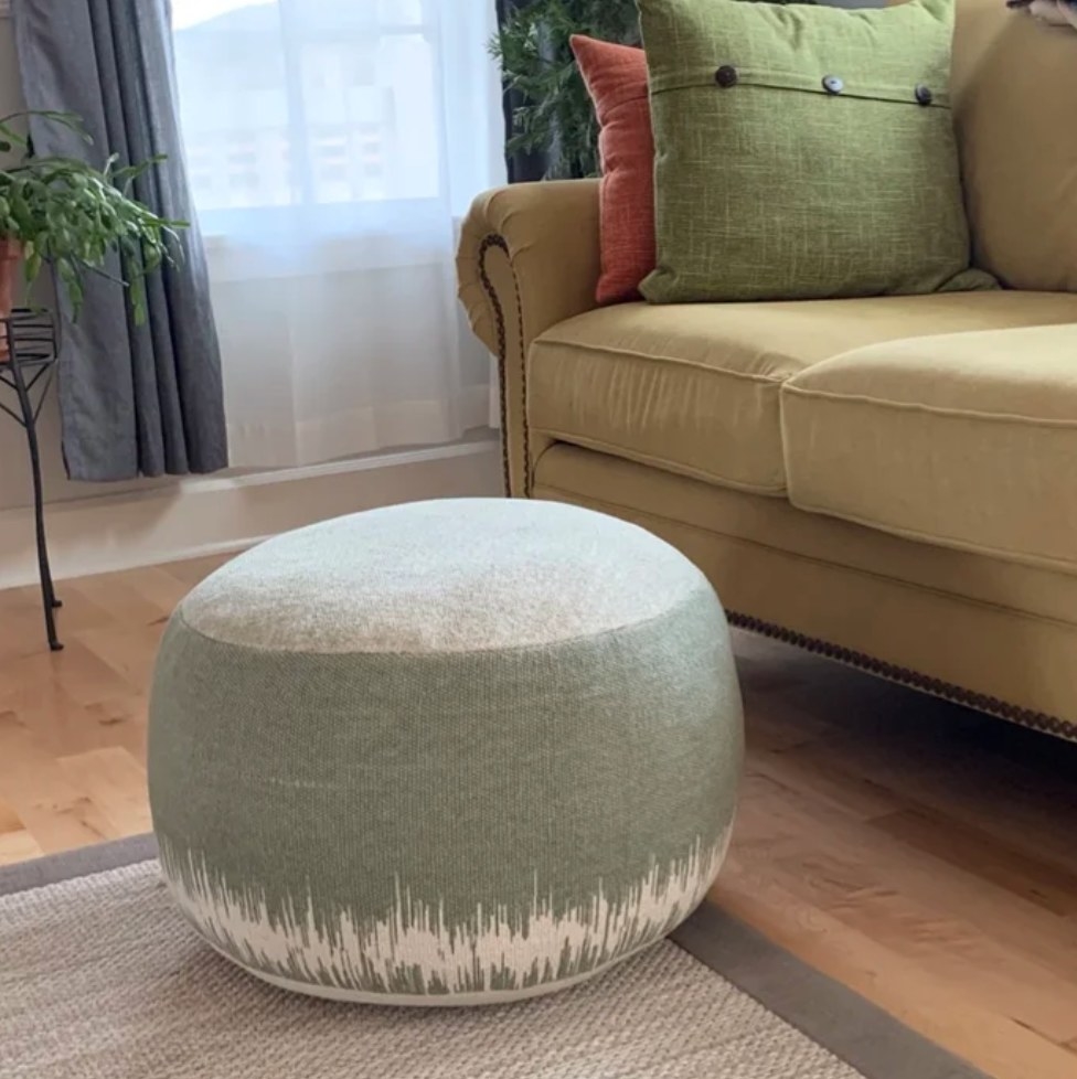 A reviewer&#x27;s round pouf in a sage green/white abstract design with a handle attached