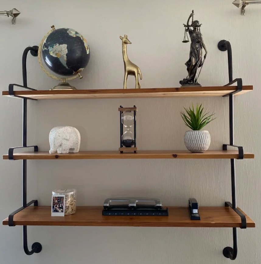 A reviewer&#x27;s three-tier wood and metal industrial wall shelf filled with decor items