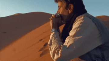 GIF of Bourdain looking pensive, sitting on a desert hilltop, watching the sunset
