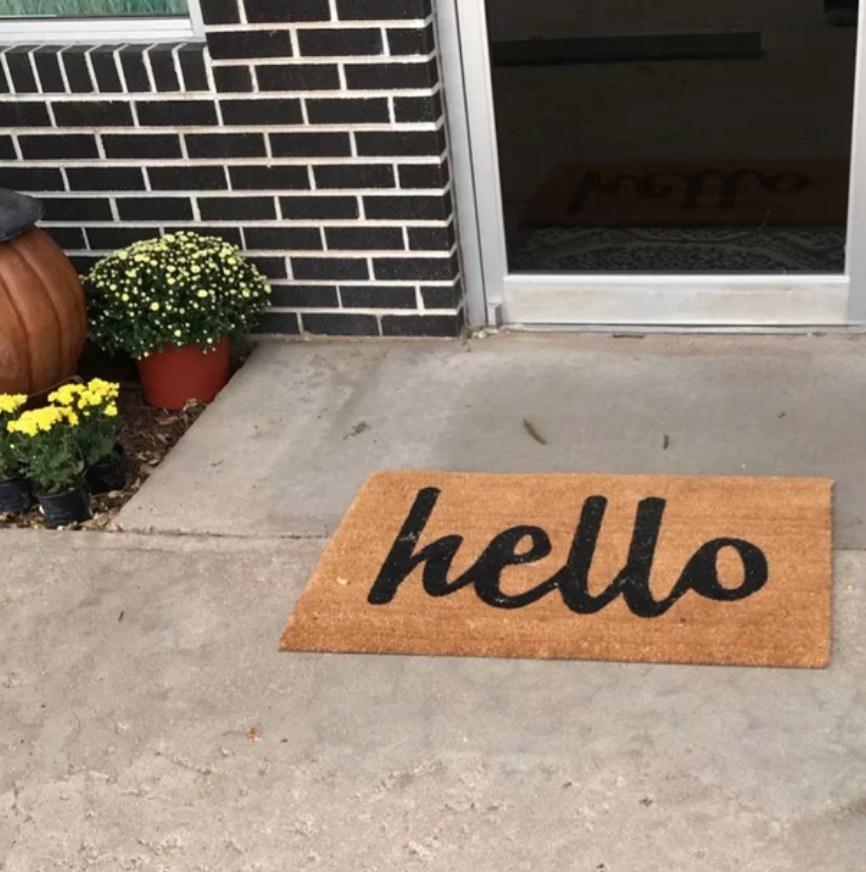 A reviewer&#x27;s tan/black, non-slip doormat that says &quot;hello&quot; placed outside a home