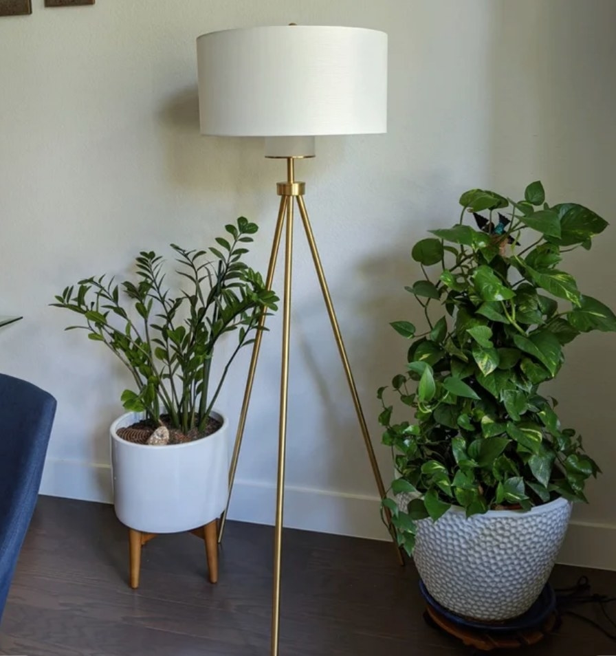 A reviewer&#x27;s tripod floor lamp with a gold base and a white fabric dome shade