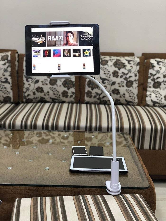 A phone/tablet holder clipped to the end of a table with the loading screen of a streaming service on it