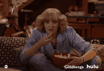 A GIF a person eating popcorn on a couch