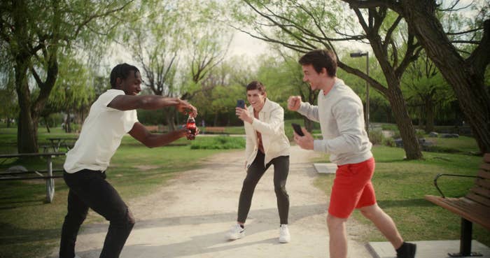Three friends hanging out in a park with one guy opening a bottle of Coca-Cola