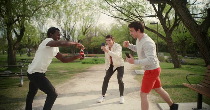 Trois amis rassemblés dans un parc et un jeune homme ouvrant une bouteille de Coca-Cola