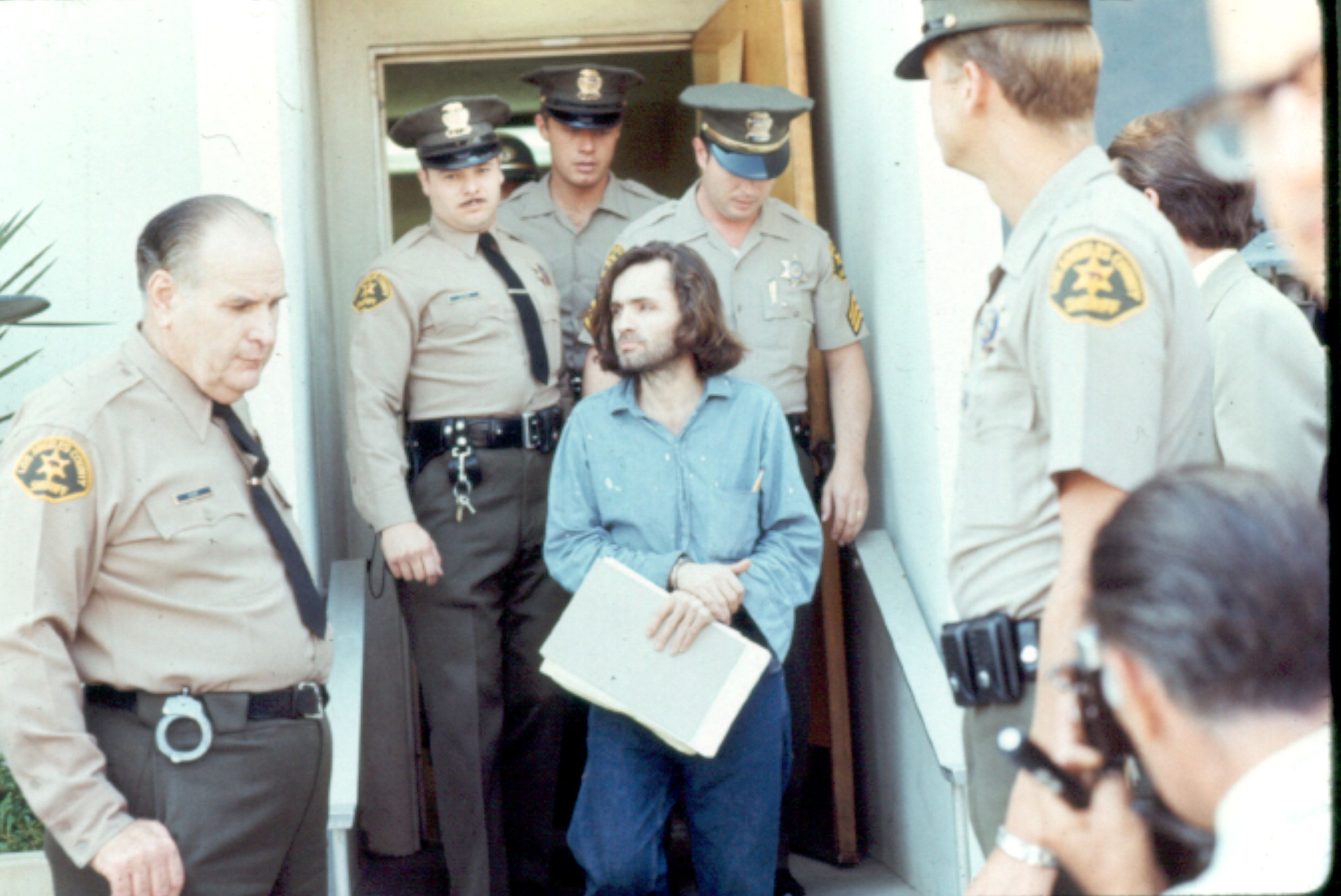 Charles Manson is escorted by several Los Angeles County sheriffs to a police van