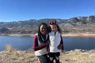 Melissa Burt poses with her young daughter in front of mountains and a lake.