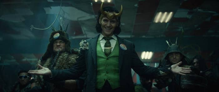 President Loki stands center, dressed in a green tux wth a horn crown