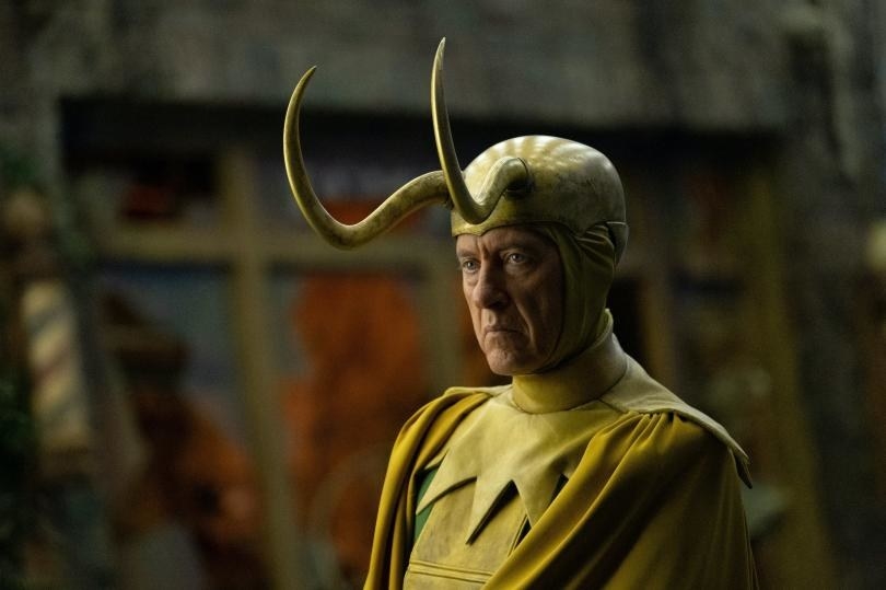 An older man wears a double horned crown and a yellow cape and yellow suit.